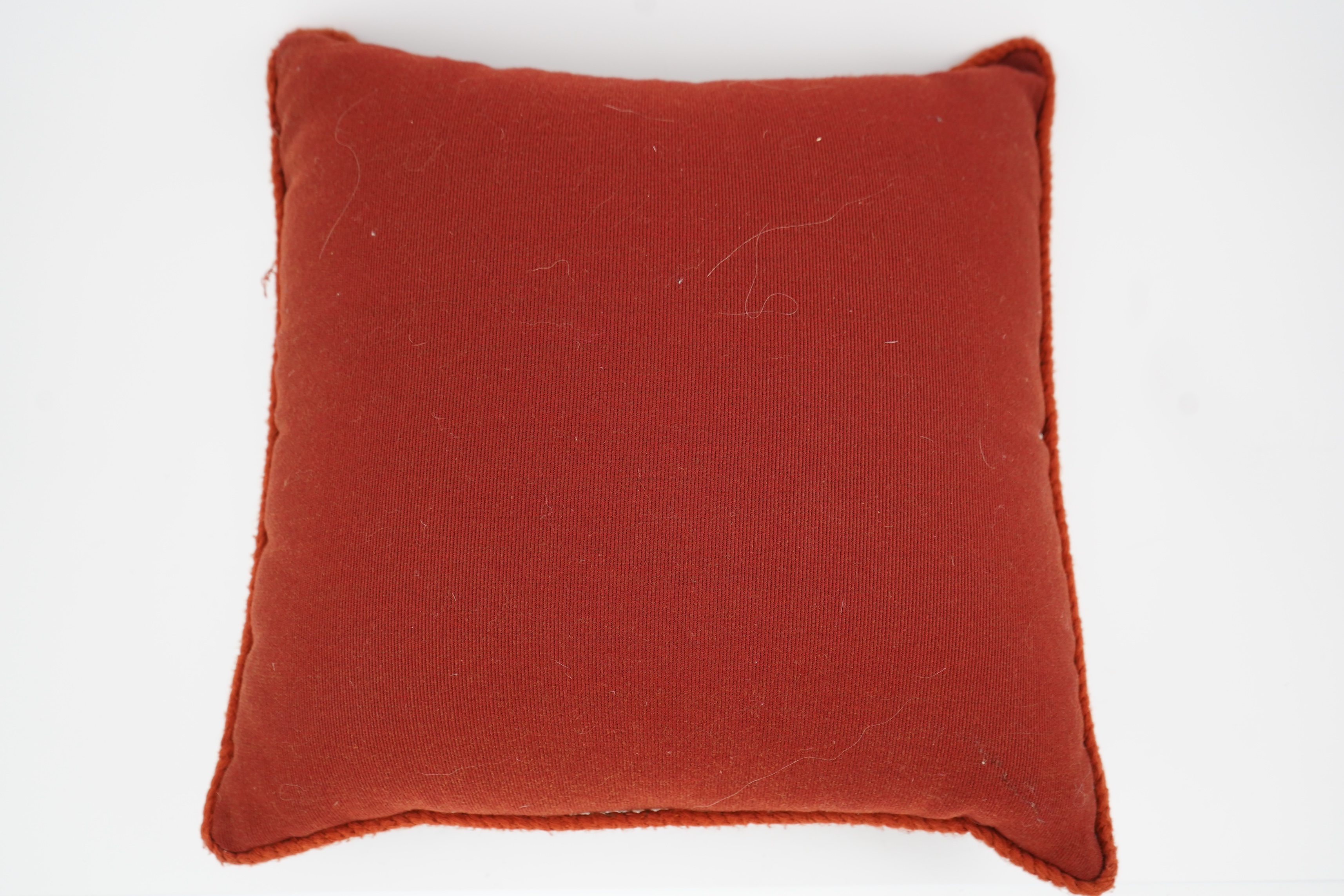 A 19th century Berlin bead worked cushion, the beadwork embroidered as a central rose, surrounded by an ornate tasseled swag, on a red wool worked background, 43cm x 45cm. Condition - some beadwork missing due to age and